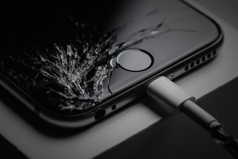 A shattered iPhone display with a frayed charging cable